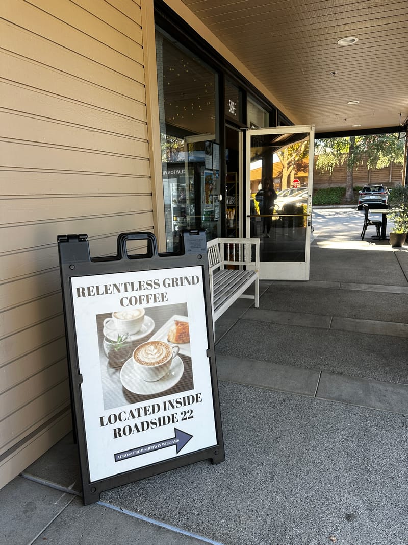 A sidewalk sign outside the door reading "Relentless Grind Coffee — located inside Roadside 22", with an arrow.