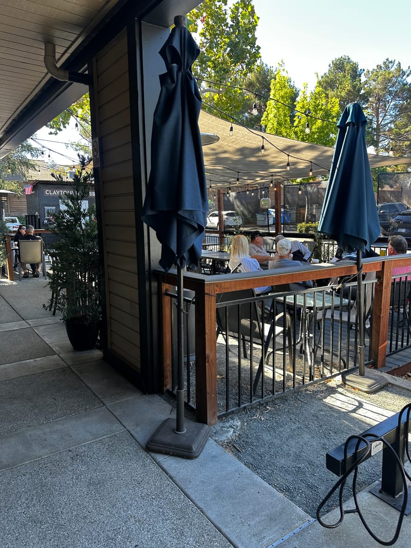The patio out front: tables and chairs behind a railing, folded umbrellas and string lights, with people at the far end.